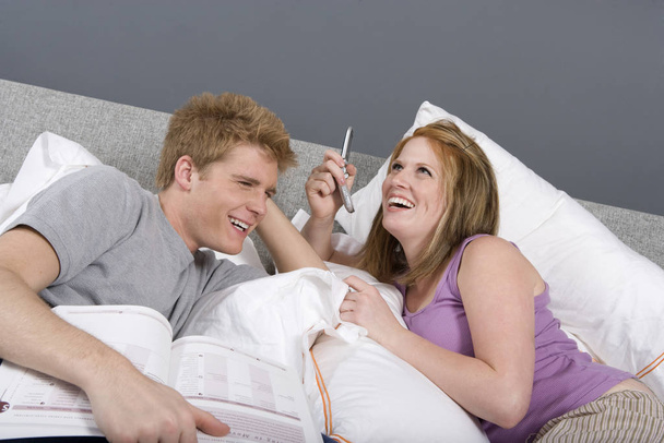 Cheerful young man with novel and woman on call in bedroom - Foto, Bild