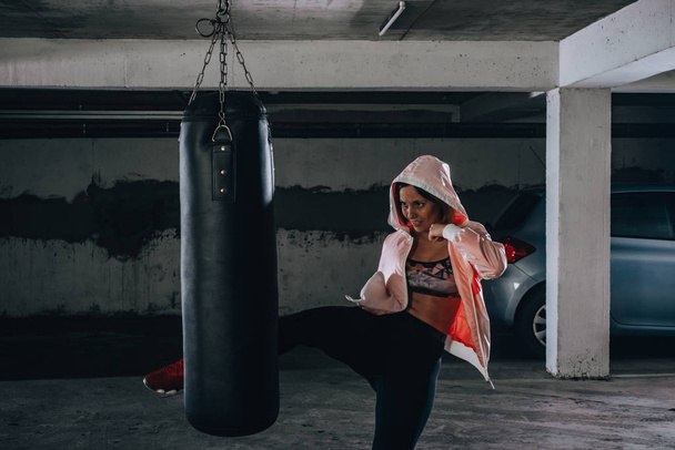 Jonge sportvrouw doet high kick tijdens het boksen oefening in een garage. - Foto, afbeelding