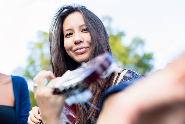Ασιατικό κορίτσι κιθάρα παίκτης που κάνει τη μουσική με τους φίλους στο πάρκο - Φωτογραφία, εικόνα