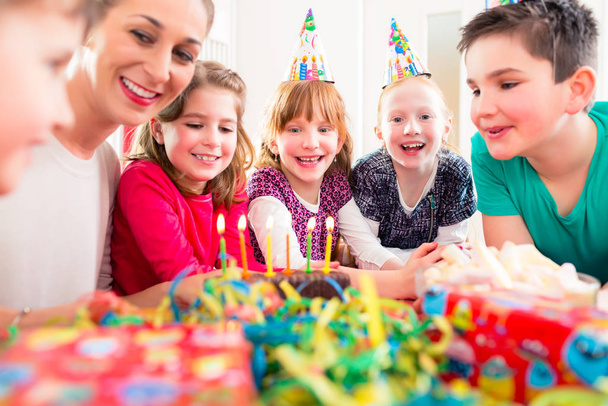 Child on birthday party blowing candles on cake being helped by friends and the mother - Photo, image