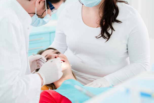 Zahnarzt behandelt Patientin in Praxis zusammen mit Zahnarzthelferin - Foto, Bild