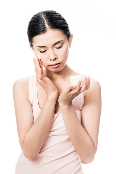 Hermosa mujer asiática joven aplicando crema humectante facial para el cuidado sensible de la piel
 - Foto, Imagen