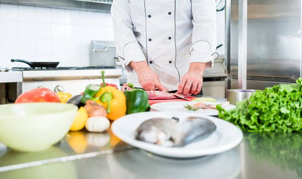 Chef preparing vegetables and fish for cooking in his kitchen - 写真・画像