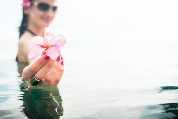 Female Tourist in infinity pool of hotel resort showing pink blossom of frangipani flower - Фото, зображення