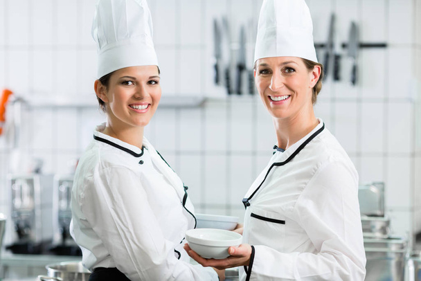 Two female chefs in gastronomic kitchen wearing white cooking uniforms - Φωτογραφία, εικόνα