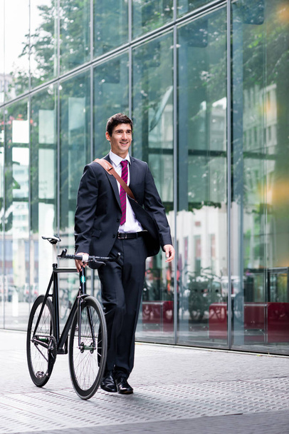 Empresário passeando de bicicleta pela cidade ao longo de uma passarela de pedestres enquanto viaja para o trabalho usando transporte ecológico
 - Foto, Imagem