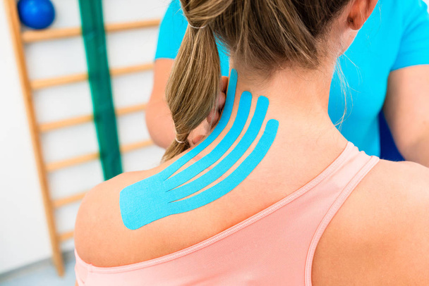 Woman from behind with Kinesio tape on shoulder in physiotherapy - Φωτογραφία, εικόνα