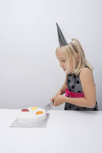 Cute girl cutting birthday cake at table in house - Fotó, kép