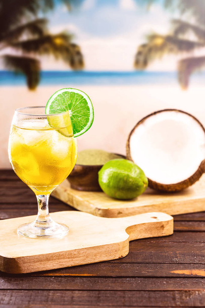 Склянка холодного напою з пляжем на задньому плані. Чай з каріокою - чай, виготовлений у Ріо - де - Жанейро. Єрба спарується і п'є з кокосовою водою та лимоном. Бразильський літній туризм. - Фото, зображення