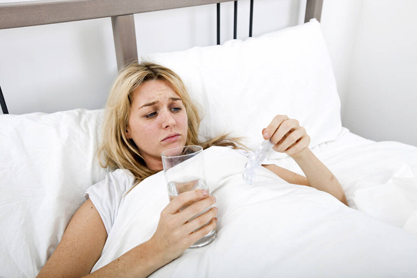 Woman suffering from cold holding water and tablet in bed - Foto, imagen