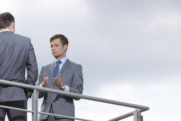Businessman gesturing while communicating with coworker against sky - Foto, immagini