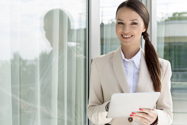 Portrait of happy businesswoman using digital tablet by glass door - Foto, afbeelding
