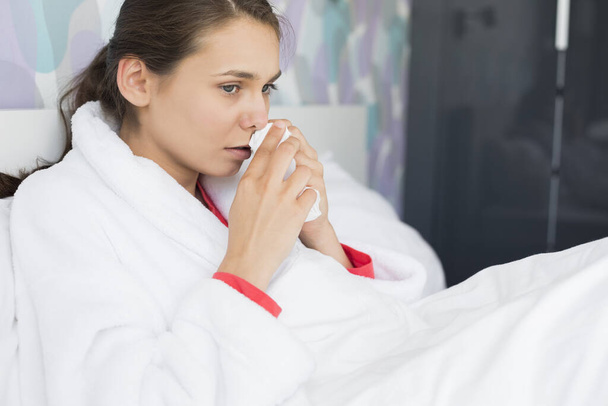Mujer joven que sufre de frío usando papel de seda en el dormitorio
 - Foto, imagen