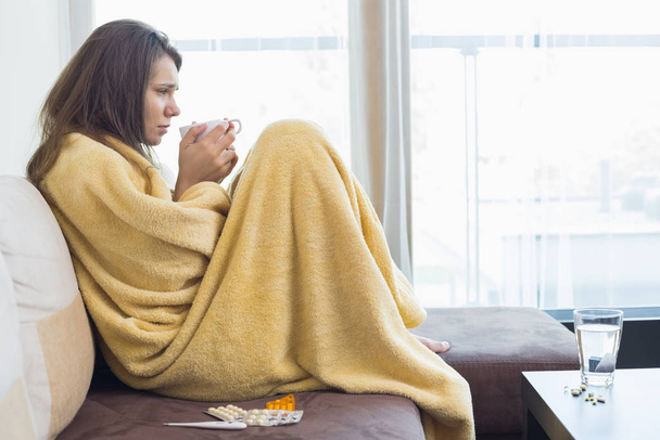 Side view of sick woman having coffee on sofa in living room - Photo, image