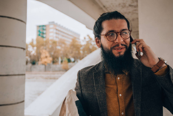 Bearded man wearing fashionable clothes talking on cellphone outdoors - 写真・画像