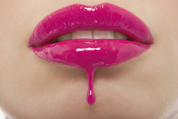 Detail shot of pink lipgloss dripping from woman's lips - Φωτογραφία, εικόνα