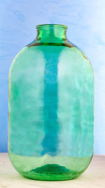 Un frasco de vidrio de 10 litros está hecho de vidrio verde grueso sobre un fondo azul
. - Foto, imagen