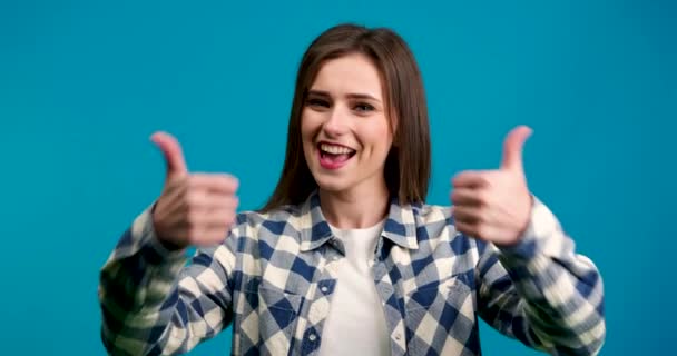Front view of smiling girl showing thumbs up and looking at camera isolated on blue background - Footage, Video