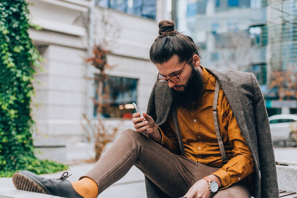 Hipster trendy guy wearing classy outfit reading a book at the city center - Foto, imagen