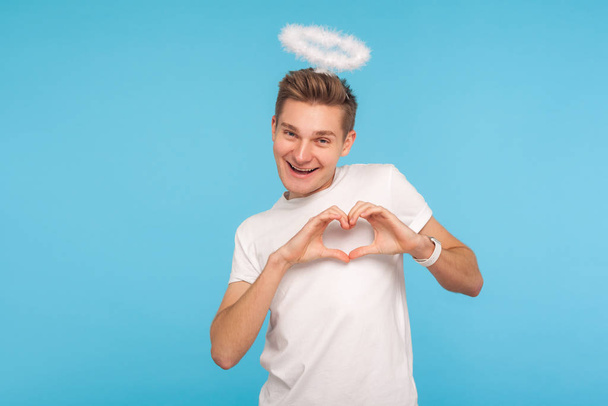 Portrait of happy angelic man with halo above head making heart  - 写真・画像