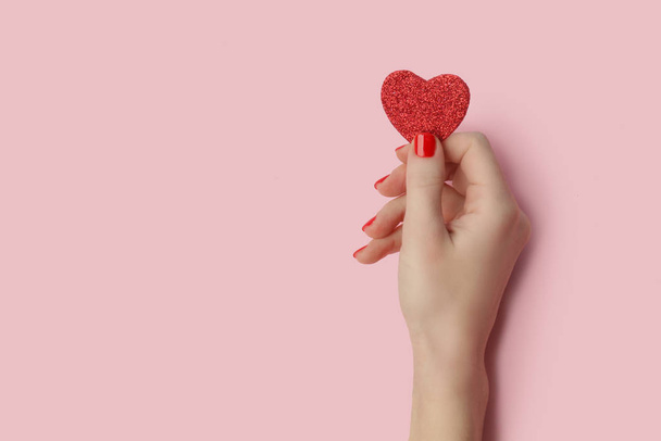 Mãos de mulher segurando coração de brilho vermelho no fundo rosa
 - Foto, Imagem