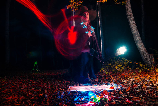 Mago (mago) lanzando un hechizo con su bastón mágico mientras está de pie en un bosque encantado. - Foto, Imagen