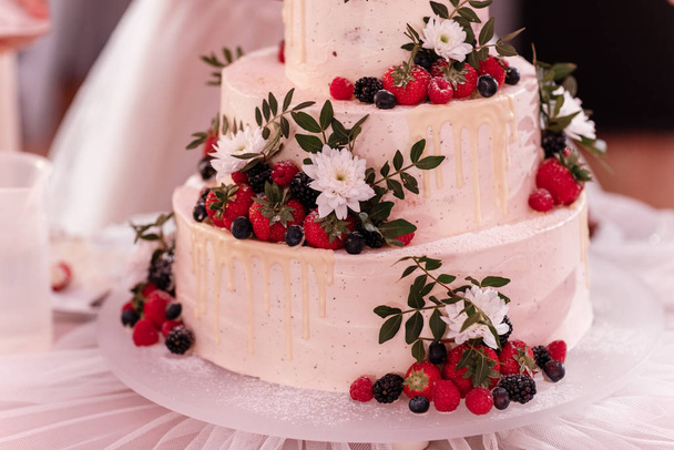 biały tort ozdobiony jagodami i białymi kwiatami na stole na weselu. dzień ślubu. - Zdjęcie, obraz