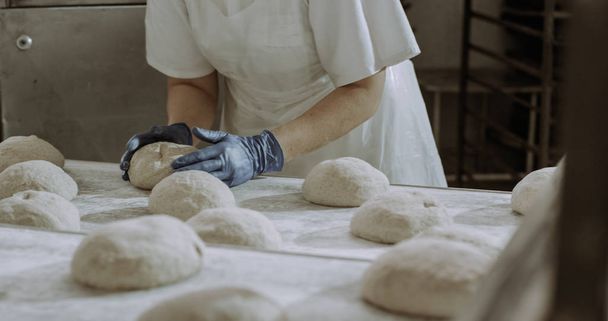 In de bakkerij commerciële keuken werken fast bakers vormen stukken deeg voor het bakken van brood in de oven ze met behulp van de - Foto, afbeelding