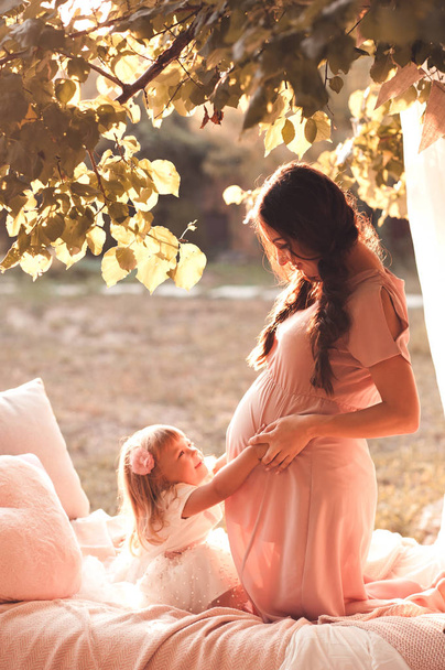Mujer embarazada con niña jugando en la cama al aire libre. Maternidad. Maternidad
.  - Foto, Imagen