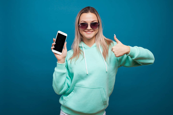 Stylish trendy hipster girl in the blue hoodie with the hood uses a smartphone. - Fotoğraf, Görsel
