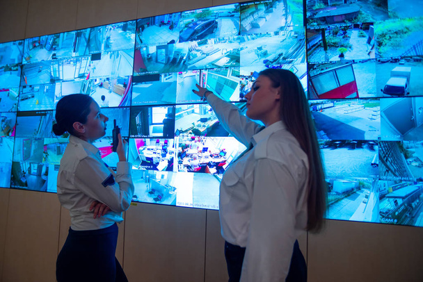 Wachleute stehen vor einem großen CCTV-Monitor im Hauptkontrollraum, während sie Pläne lesen und diskutieren - Foto, Bild