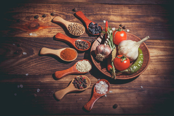 Different spices in wooden spoons and different ingredients for cooking, cherry tomatoes, garlic, coriander and red pepper - Fotografie, Obrázek