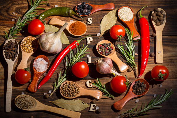 Different spices in wooden spoons and different ingredients for cooking, cherry tomatoes, garlic, coriander and red pepper - Foto, immagini