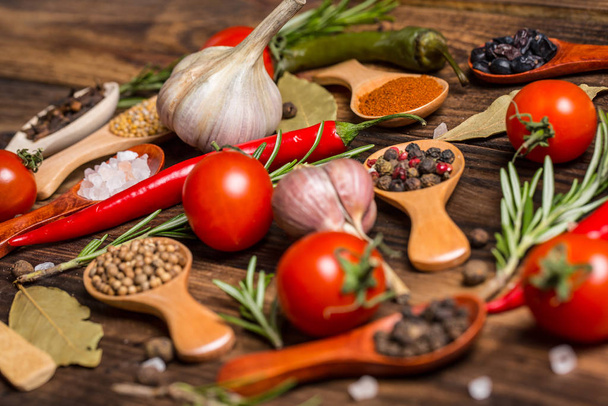 Different spices in wooden spoons and different ingredients for cooking, cherry tomatoes, garlic, coriander and red pepper - Foto, afbeelding