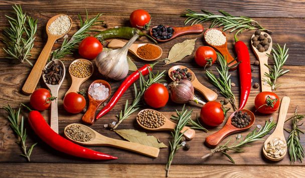 Różne przyprawy w drewnianych łyżeczkach i różnych składnikach do gotowania, pomidory wiśniowe, czosnek, kolendra i pieprz czerwony - Zdjęcie, obraz