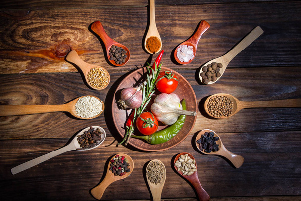 Different spices in wooden spoons and different ingredients for cooking, cherry tomatoes, garlic, coriander and red pepper - Photo, Image