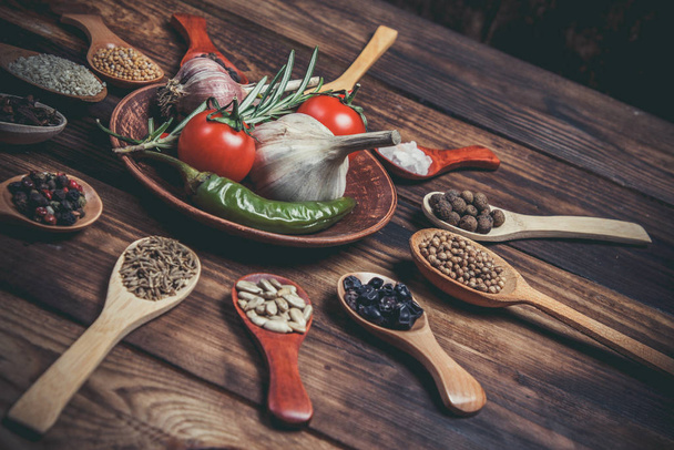 Different spices in wooden spoons and different ingredients for cooking, cherry tomatoes, garlic, coriander and red pepper - 写真・画像