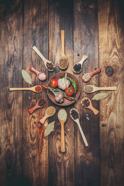 Diverse spezie in cucchiai di legno e diversi ingredienti per la cottura, pomodorini, aglio, coriandolo e peperoncino
 - Foto, immagini