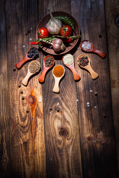 Different spices in wooden spoons and different ingredients for cooking, cherry tomatoes, garlic, coriander and red pepper - Photo, image