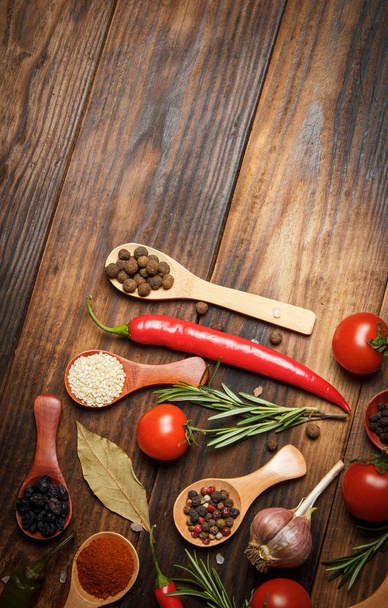 Different spices in wooden spoons and different ingredients for cooking, cherry tomatoes, garlic, coriander and red pepper - 写真・画像