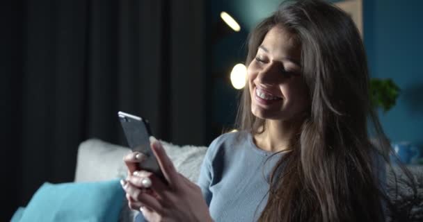 Pretty young lady texting with smartphone on couch - 映像、動画