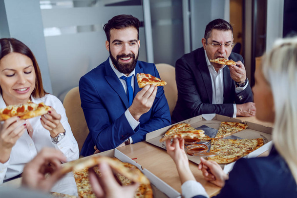 役員室に座っている間に昼食のためのピザを持っている空腹のビジネスの人々のグループ. - 写真・画像