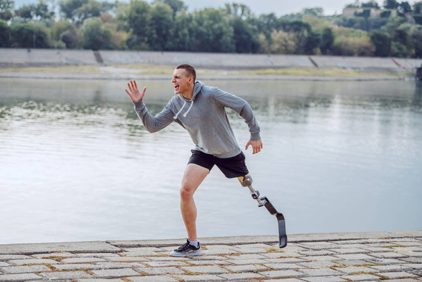 Side view of healthy caucasian handicapped sportsman in sportswear and with artificial leg running on quay. - Photo, Image
