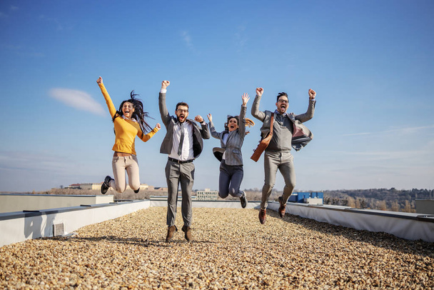 Cuatro felices empresarios emocionados saltando en la azotea y animando por el éxito
. - Foto, Imagen