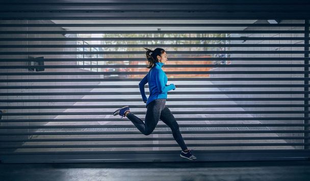 Fiatal fitt vonzó kaukázusi sportos nő melegítőben fut gyorsan a garázsban. A városi élet fogalma. - Fotó, kép