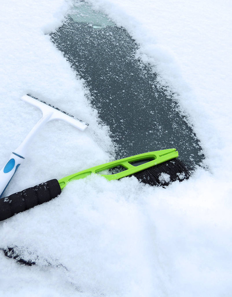 Кисть и скребок в снегу на лобовом стекле автомобиля. Инструменты для очистки автомобилей от снега
.      - Фото, изображение