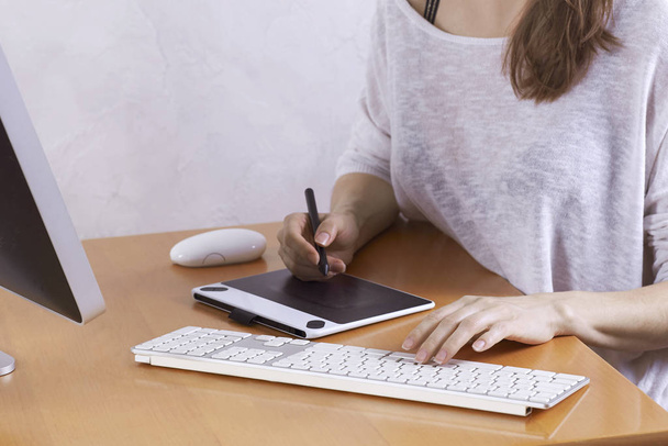 The hands of young woman, artist or graphic designer, drawing on graphic tablet and using wireless keyboard and mouse at home office. Woman freelance. Indoors, copy space. - Foto, afbeelding
