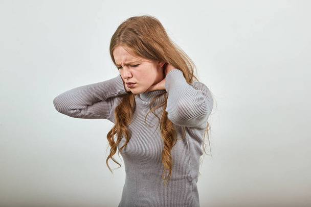 mujer en suéter con el pelo rojo se dobla en el dolor, sosteniendo su dolor de cuello y garganta
 - Foto, Imagen