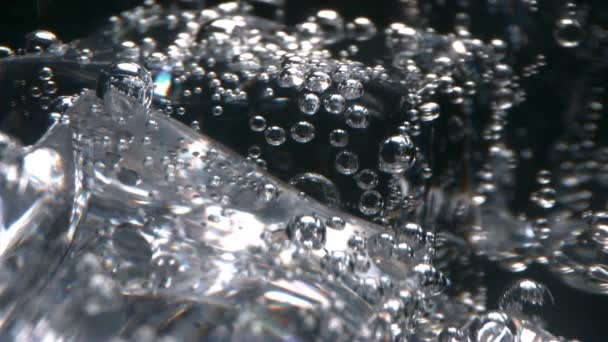 Szénsavas víz egy makró buborékok lebeg jéggel egy pohár fekete háttér  - Felvétel, videó