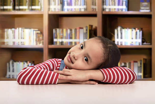Beautiful asian little girl lying down on the desk resting at library - Zdjęcie, obraz